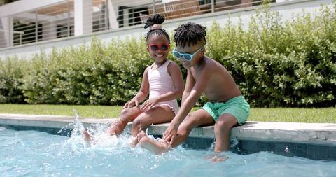 Playful siblings splashing water at poolside getaway