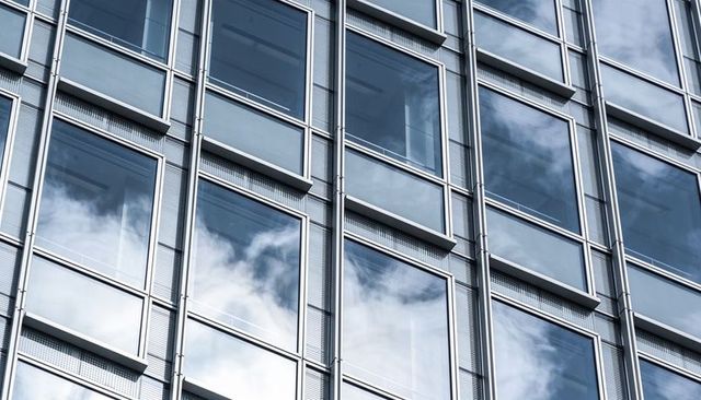 Glass curtainwall reflecting clouds, window panels and metal mullions on office skyscraper