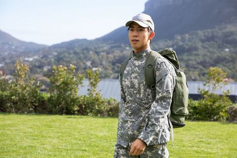 Young asian soldier walking with olive rucksack on training field with mountain valley
