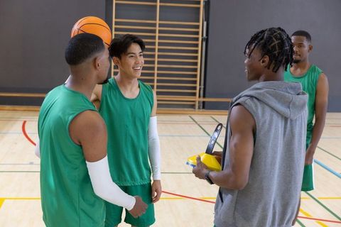 Multiracial basketball team huddling while coach holding timer during indoor practice
