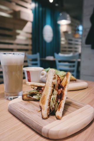 Toasted Club Sandwich with Bacon and Latte on Wooden Board in Cozy Cafe