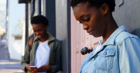 Twin Sisters Standing with Mobile Phones in Urban Street View