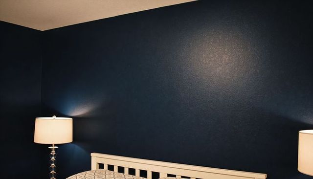 Cozy navy bedroom interior featuring white slatted headboard, glass lamps, patterned quilt