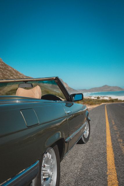 Convertible car parked on an empty coastal road with mountains and ocean in the background. Ideal for travel blogs, vacation advertisements, road trip promotions, and scenic journey themes.
