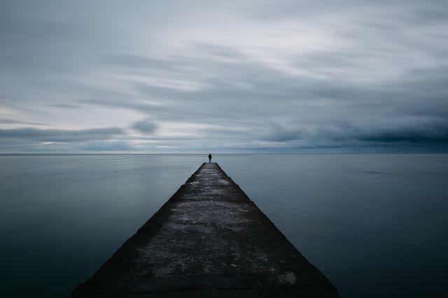 Solitary Figure on Pier Gazing at Overcast Sea - Download Free Stock Photos Pikwizard.com