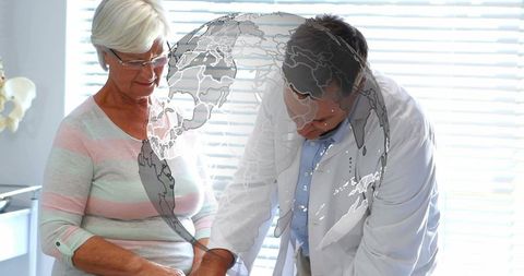 Doctor examining senior woman's wrist during consultation in bright clinic with globe overlay