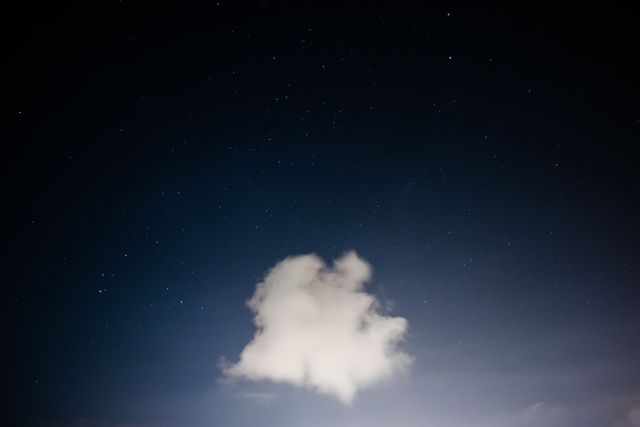 A single fluffy white cloud is isolated against a backdrop of a beautifully starry night sky with noticeable dark blue hues. This image exudes tranquility and serenity, making it perfect for themes of solitude, peace, nature, and calm. It is also suitable for use in astronomy meetings or presentations, and for materials related to weather or the night-time environment.