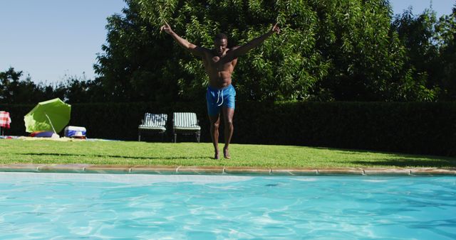 This image of a young man diving into a swimming pool captures the excitement and joy of summer outdoor activities. Ideal for use in advertisements, travel brochures, websites promoting summer vacations and leisure activities, fitness blogs, or content related to fun, relaxation, and healthy lifestyle promoting outdoor activities. The vibrant greenery and blue water emphasize a refreshing and energetic atmosphere.