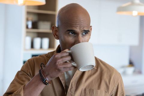 African american man sipping morning coffee in home kitchen, contemporary, relaxed and thoughtful