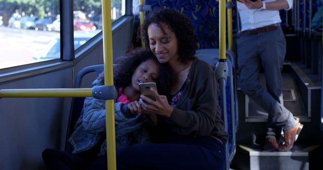 Happy african american mother and daughter sitting in city bus using smartphone. Communication, transport, city living and senior lifestyle, unaltered.