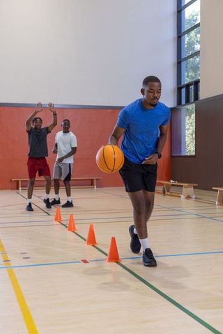 Three african american men dribbling basketballs through cone drill in indoor gym