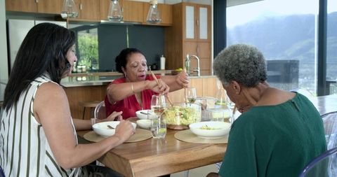 African american women serving salad at kitchen table during family gathering