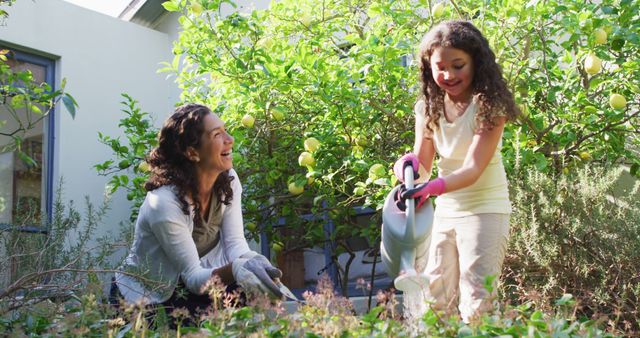 Biracial mother and daughter gardening in sunny garden, watering plants. domestic life and family leisure time concept.