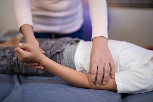 Close-up of female therapist examining hand while boy lying on bed at hospital ward
