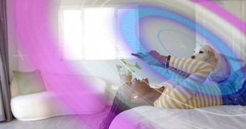 Woman Enjoys Leisure Time with Smartphone and Dog on Cozy Bed