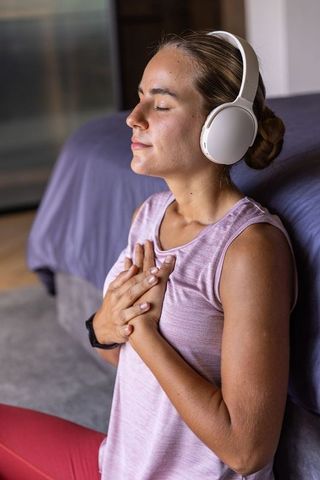 Woman meditating with headphones in bedroom practicing mindfulness breathwork for relaxation