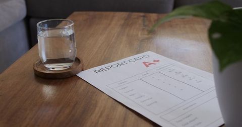 Report card showing a+ on wooden table with glass of water and potted plant, cozy minimal