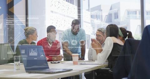 Leader leaning over meeting table, diverse team brainstorming with laptop and analytics