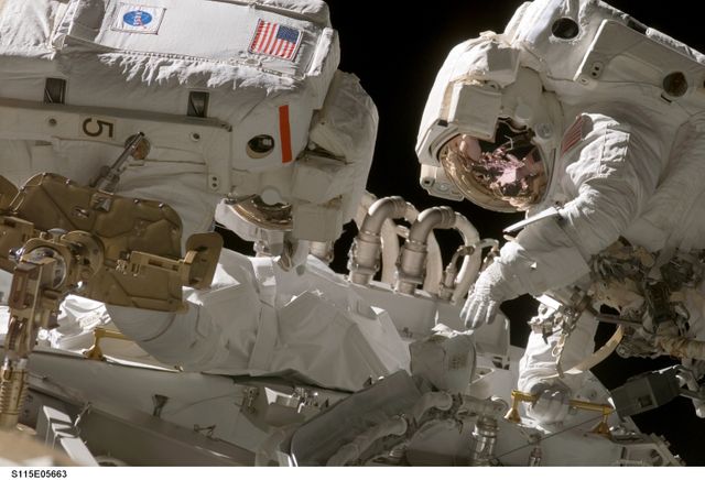 Two astronauts working on power cables and Solar Alpha Rotary Joint during a spacewalk on the STS-115 mission in 2006. This image is excellent for educational materials, presentations on space missions, and articles about space exploration.