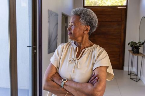 Senior african american woman standing arms crossed looking out glass door in modern entry