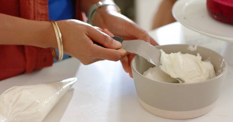 Woman scraping creamy buttercream from bowl with spatula for cake decorating