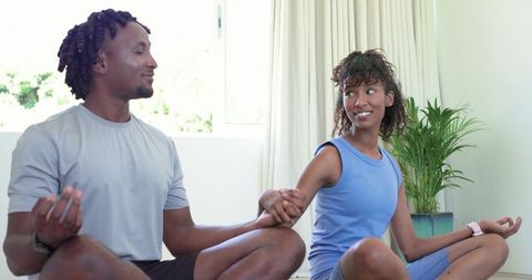 Couple practicing partner meditation and yoga in sunlit minimalist home holding hands