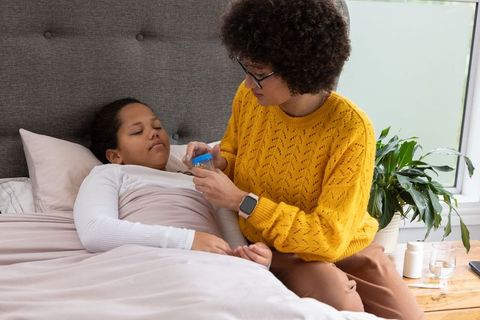 African american mother caring for sick daughter in bed holding medicine bottle