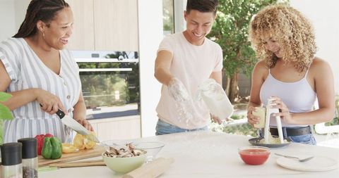 Diverse friends cooking pizza laughing and bonding in kitchen
