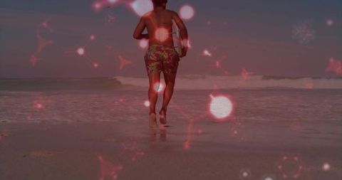 Walking man carrying tablet on wet sand at sunset with red bokeh overlay