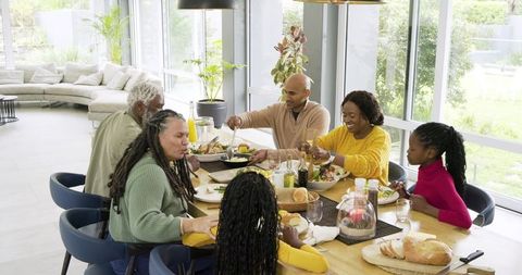 Multigenerational family enjoying sunlit meal around modern wooden dining table