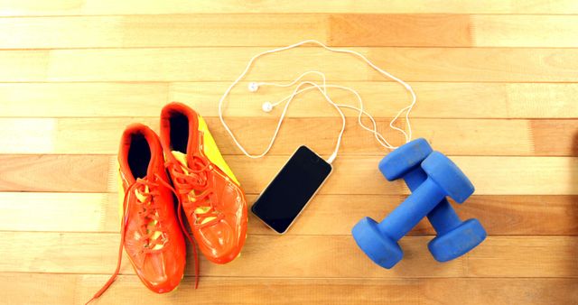 Bright sports shoes, blue dumbbells, and a smartphone with earbuds placed on a wooden floor, representing gym and fitness essentials. Ideal for advertisements on sports gear, fitness programs, gym promotions, or healthy lifestyle blogs.