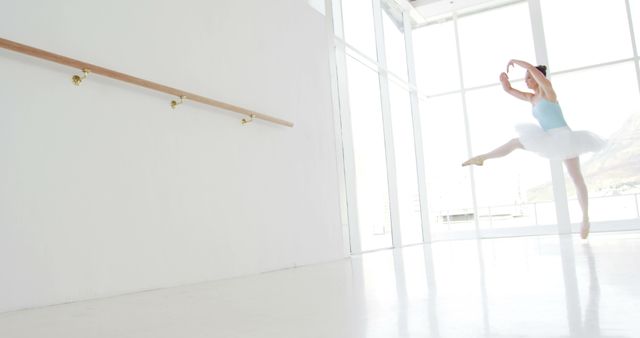Ballet dancer leaping gracefully in well-lit, pristine studio with ballet barre in background. Bright, open space highlighting dancer's skill and technique. Ideal for articles on dance, ballet advertisements, or promoting dance schools and ballet classes.