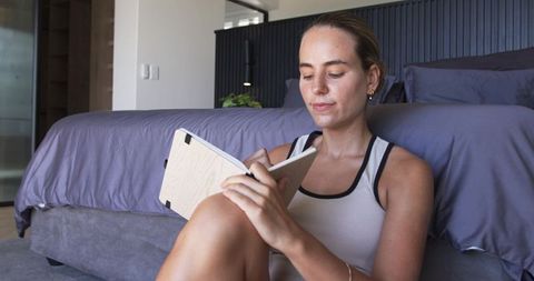 Young woman journaling on bedroom floor, writing in wooden notebook, modern cozy scene