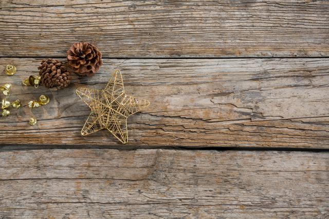 Christmas ornaments, including gold bells, pine cones, and a star, displayed on a rustic wooden plank, perfect for holiday greetings, festive backgrounds, and decoration inspirations.