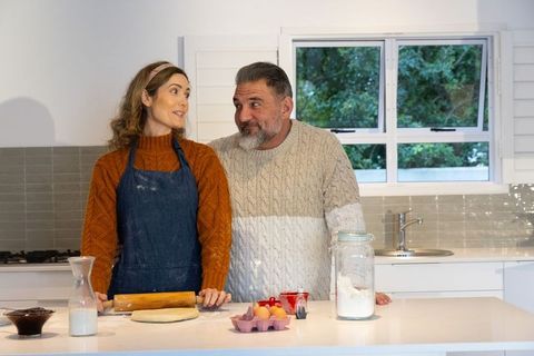 Middle-aged couple baking together in cozy kitchen rolling dough and sharing warm moment