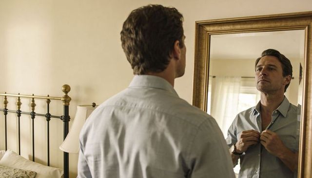 Buttoning light-blue shirt while checking collar in mirror for smart casual look