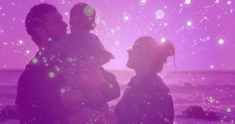 Silhouette of Family Enjoying Coastal Sunset with Pink Bokeh Effects