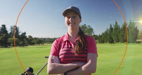 Confident female golfer smiling on fairway wearing pink striped polo and grey cap