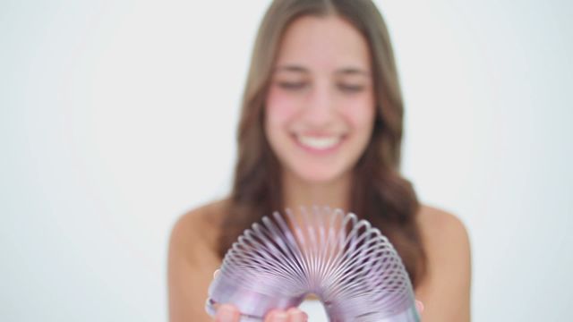 Happy brunette woman playing with a metal spring against a white background