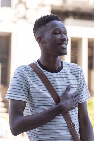Young man smiling with hand on chest wearing striped t-shirt and crossbody bag in city