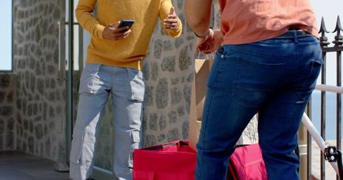 Two men sharing luggage and checking smartphone on stone balcony during travel pickup