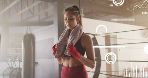Female boxer pausing between rounds holding towel wearing red hand wraps in boxing ring