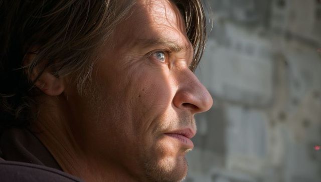 Contemplative stubbled man gazing through window soft natural light profile portrait warm texture