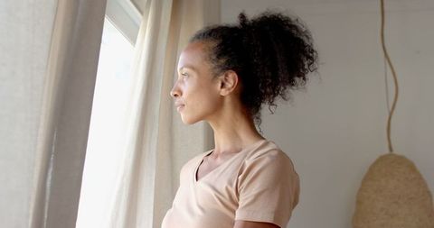 Thoughtful woman gazing out window illuminated by natural light