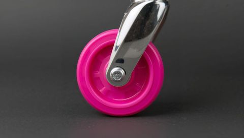 Showing bright pink plastic caster wheel in chrome swivel fork closeup on gray backdrop
