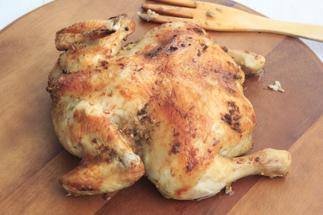 Golden roasted whole chicken resting on a wooden cutting board. Perfect for use in food blogs, culinary tutorials, and menus. Captures the essence of home-cooked meals and hearty, delicious dinners.