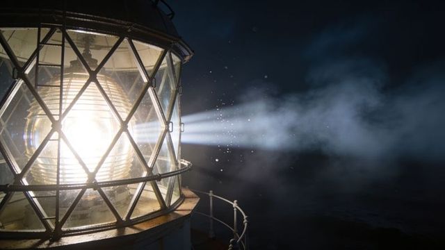 Fresnel lighthouse lens emitting powerful beam through night mist and sea spray