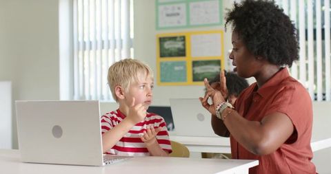 Inclusive teacher signing to student in classroom, sign language lesson with laptop