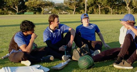 Young cricket team resting on grass in blue kit, chatting and bonding after practice
