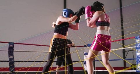 Female boxers sparring in ring trading punches with referee watching